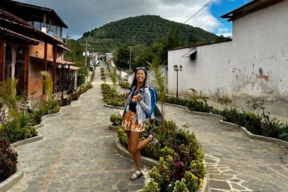 A woman standing outside on a pedestrian-street surrounded by bushes.