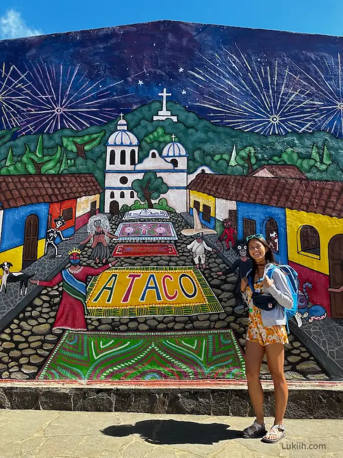 A woman standing next to a colorful mural that says ATACO.