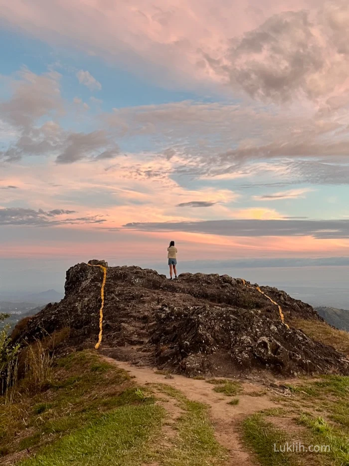 A woman on a rock looking out at a pink sky during sunset time.