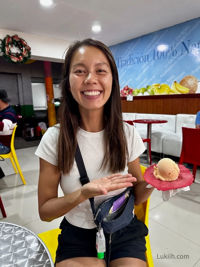 A woman holding a red edible waffle with a scoop of orange ice cream.