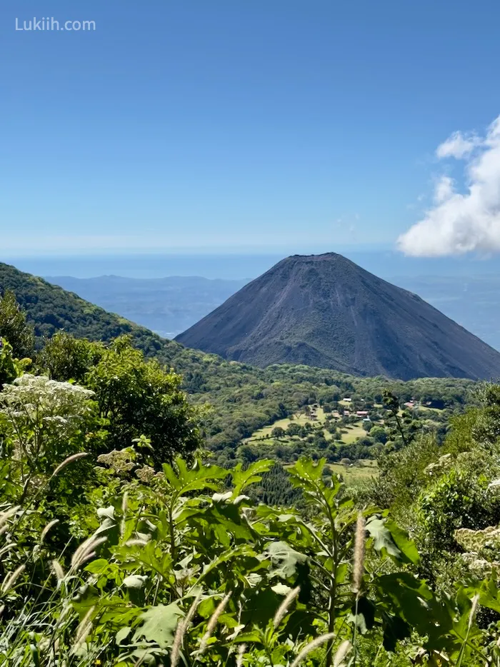 The peak of a volcano peaking out over a lush tropical mountain.