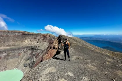 A woman standing on a volcano ridge with a view of lakes on both sides.