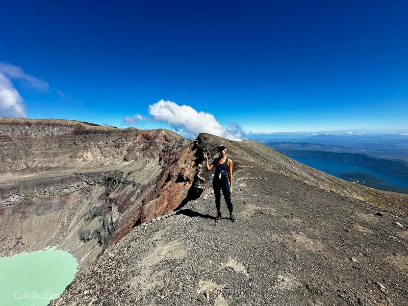 A woman standing on a volcano ridge with a view of lakes on both sides.