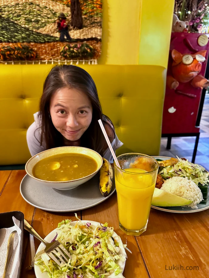 A woman sitting next to a large bowl of soup and plate.