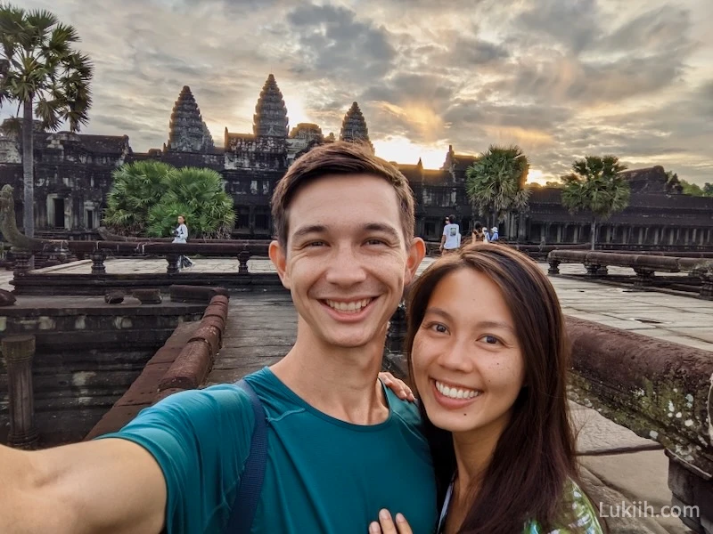 A couple smiling with a sacred, ornate building with three peaks in the background.