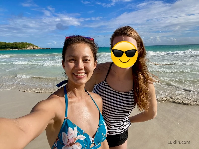 Two women taking a selfie next to a sandy beach.