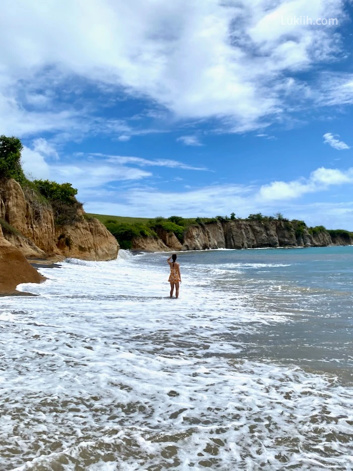 A woman standing on a beach looking at the cliffs.