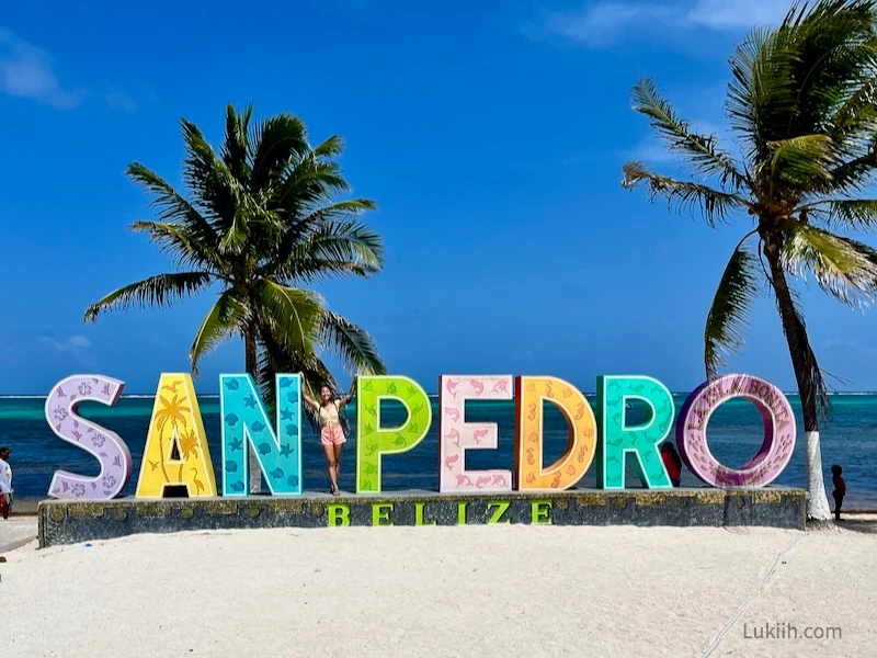 A woman posing with a SAN PEDRO sign with sand and palm trees.