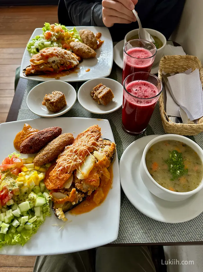 A table full of vegan food, including an eggplant dish, soup, red juice, and cake.