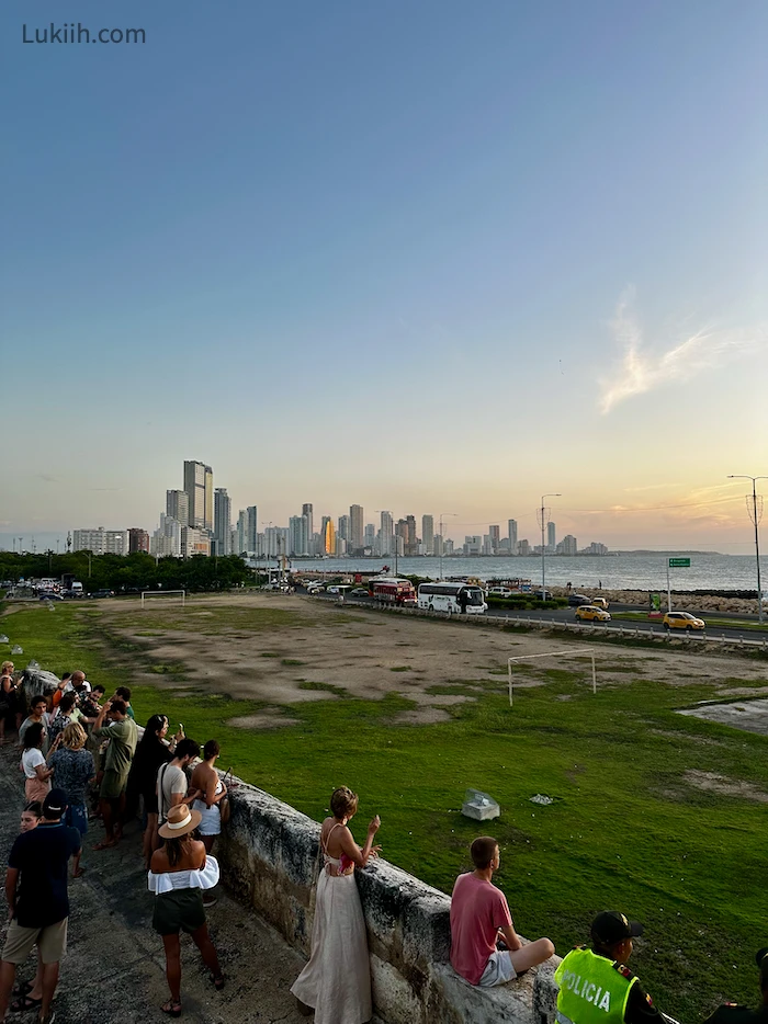 People lined against a wall, looking out a sunset.