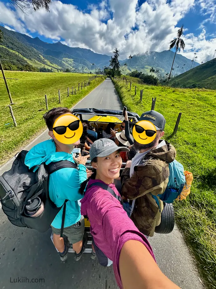 A woman riding at the back of a jeep while standing up and holding on.