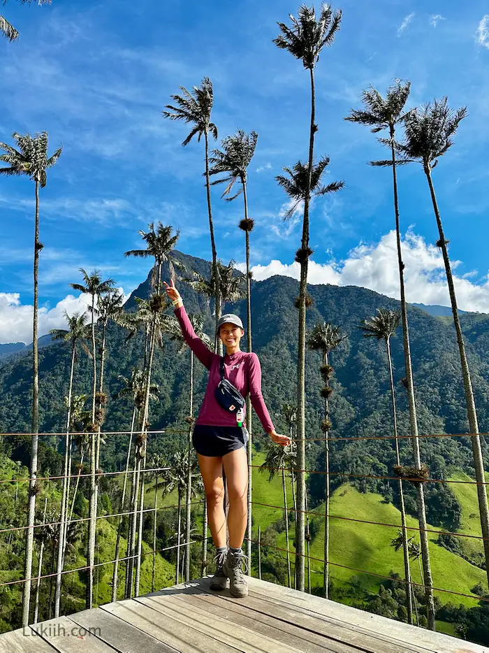 A woman standing on an wooden platform with towering palm trees behind her.