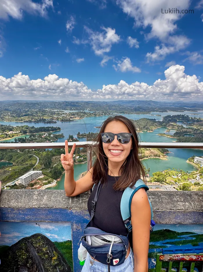 A woman throwing up a peace sign overlooking a stunning lake.