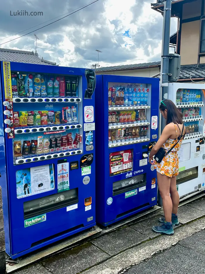 A woman standing by many vending machines with drinks in them.