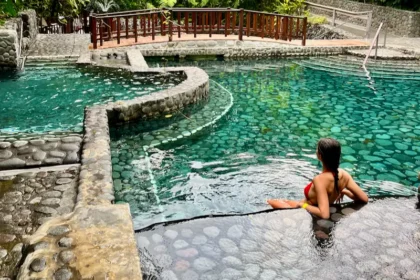 A woman leaning in a quiet pool with a bridge and lush trees in the background.