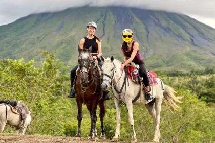 Two people riding horses with a volcano in the background.