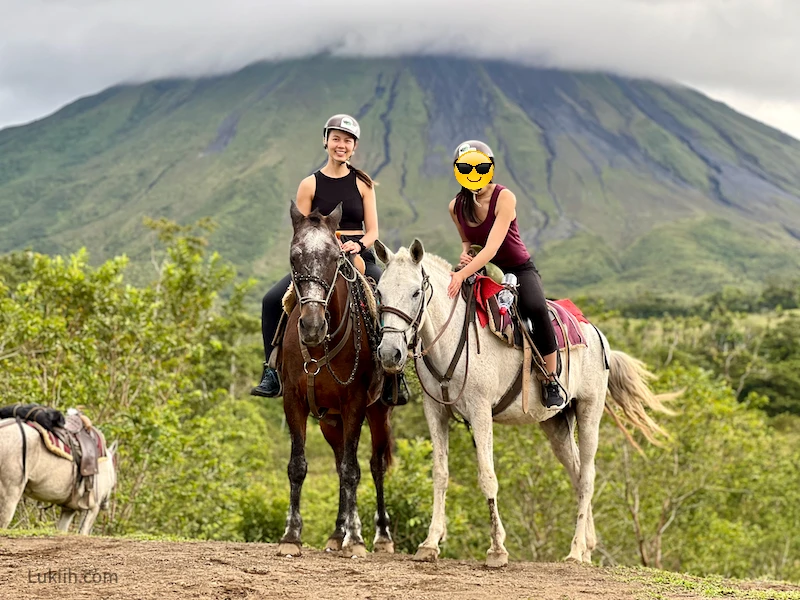 Two people riding horses with a volcano in the background.