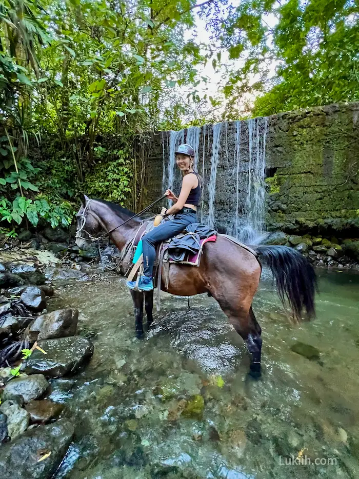 A woman riding a horse through a creek.