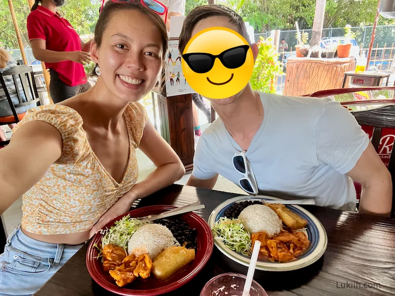 Two people eating a plate of food with rice, salad, protein and beans.