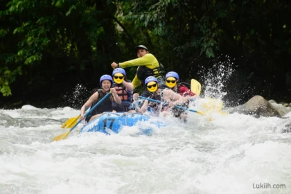 Five people on a raft rafting through a river with a lot of splash.