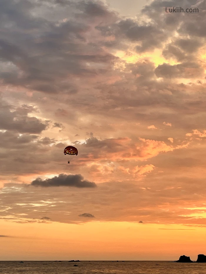 A vivid, orange sunset at a beach with someone paragliding.