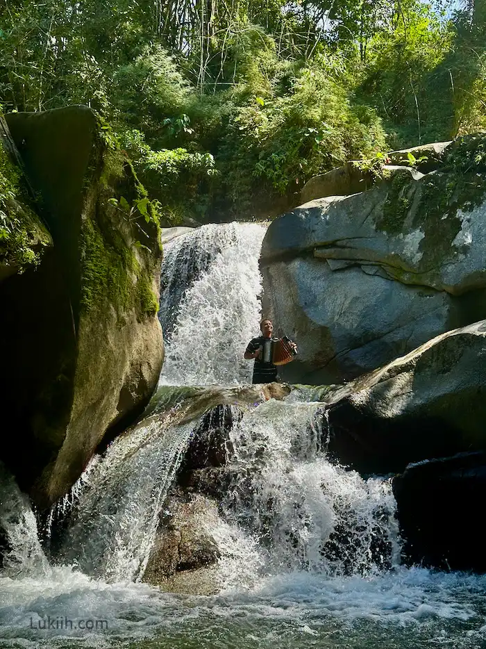 An accordian player playing inside a waterfall.