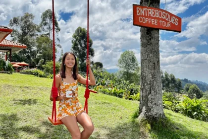 A woman sitting on a swing, holding a cup of coffee, at a coffee farm.