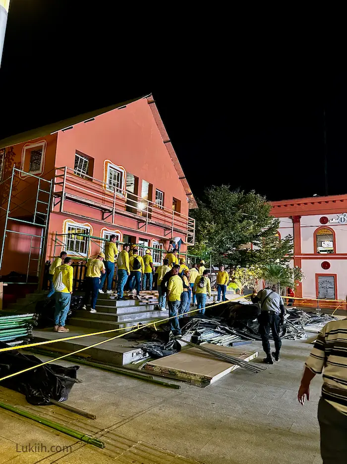 A dozen men dressed in yellow working on a building.