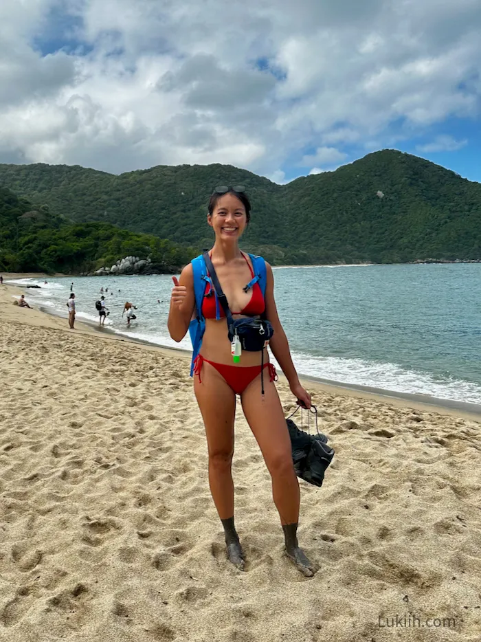 A woman standing on a sandy beach with mud covering a bit past her angle.