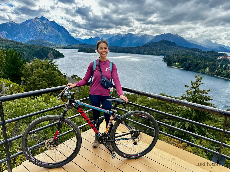 A woman with a mountain bike at a viewpoint overlooking a lake and mountain.