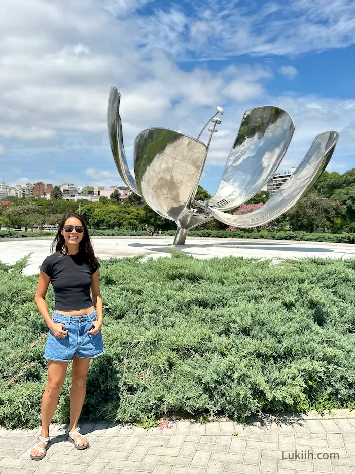 A woman standing in front of a large metallic flower sculpture.